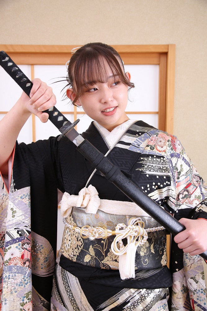 成人式の前撮り撮影で刀を持ってポーズをとる黒い古典柄の振袖を着た女性